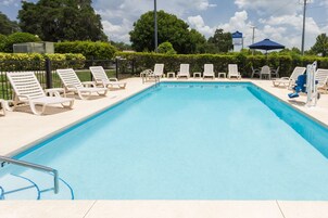 Una piscina rectangular con superficie de agua azul cristalina, rodeada de sillas de descanso blancas y una valla negra.