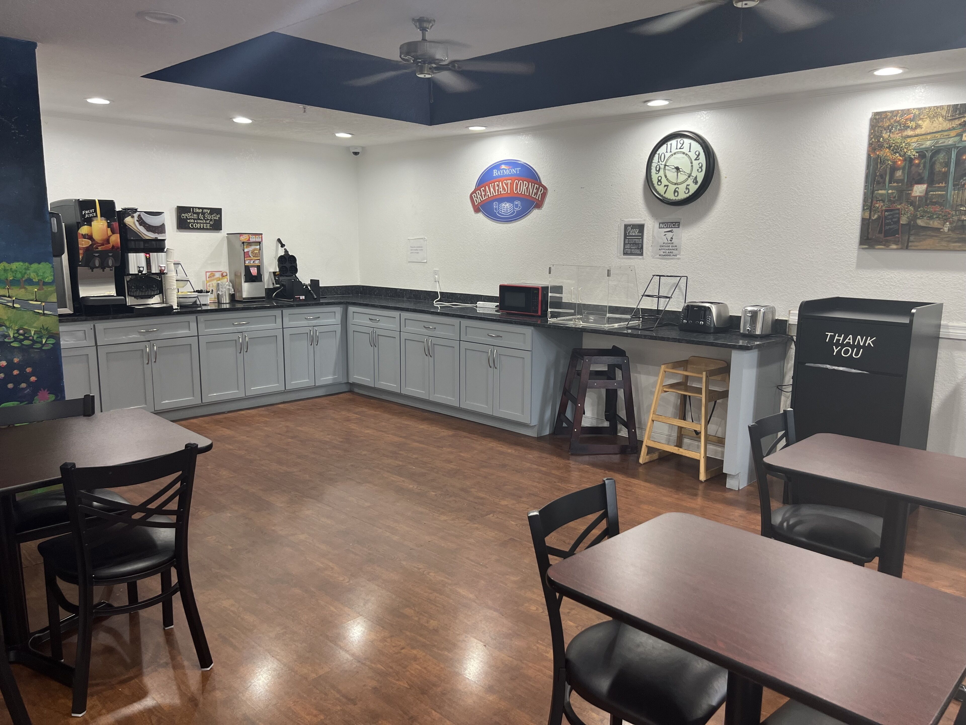 A modern kitchen with grey cabinets, a coffee station, a clock, and a 'Breakfast Corner' sign.
