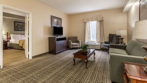 A hotel room with a bed, a television, a sofa, a coffee table, and a window with curtains.