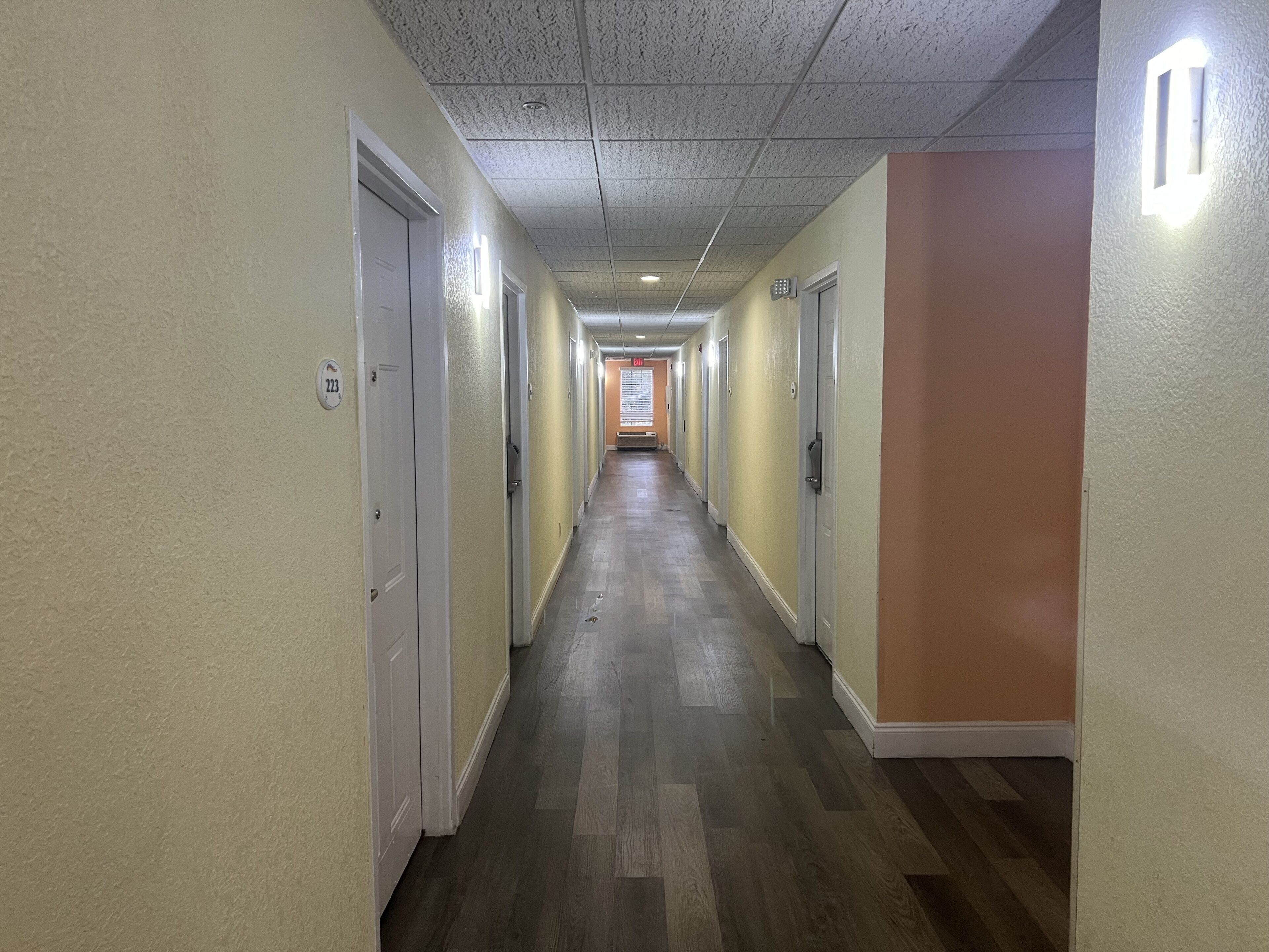 Un long couloir étroit, avec des portes de chaque côté, un plafond orné de motifs et une bande lumineuse fixée au mur.