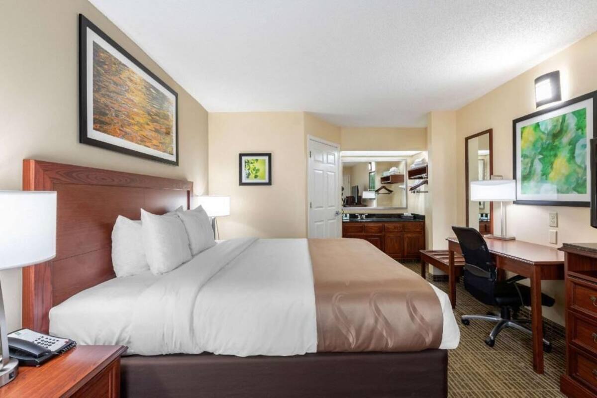 Quarto de hotel com cama, escrivaninha, cadeira e espelho.