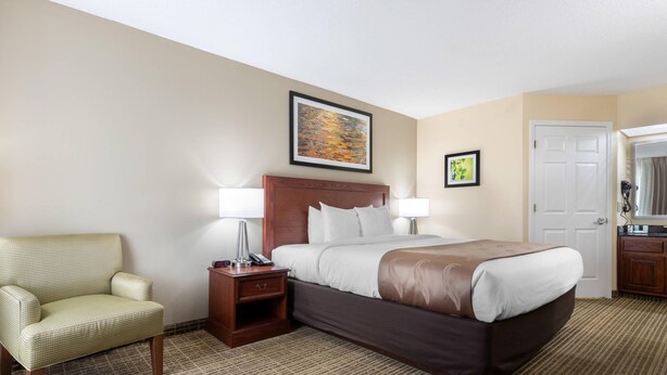 Una habitación de hotel con una cama, una silla, una mesita de noche y una puerta.