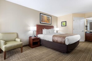 Una habitación de hotel con una cama, una silla, una mesita de noche y una puerta.