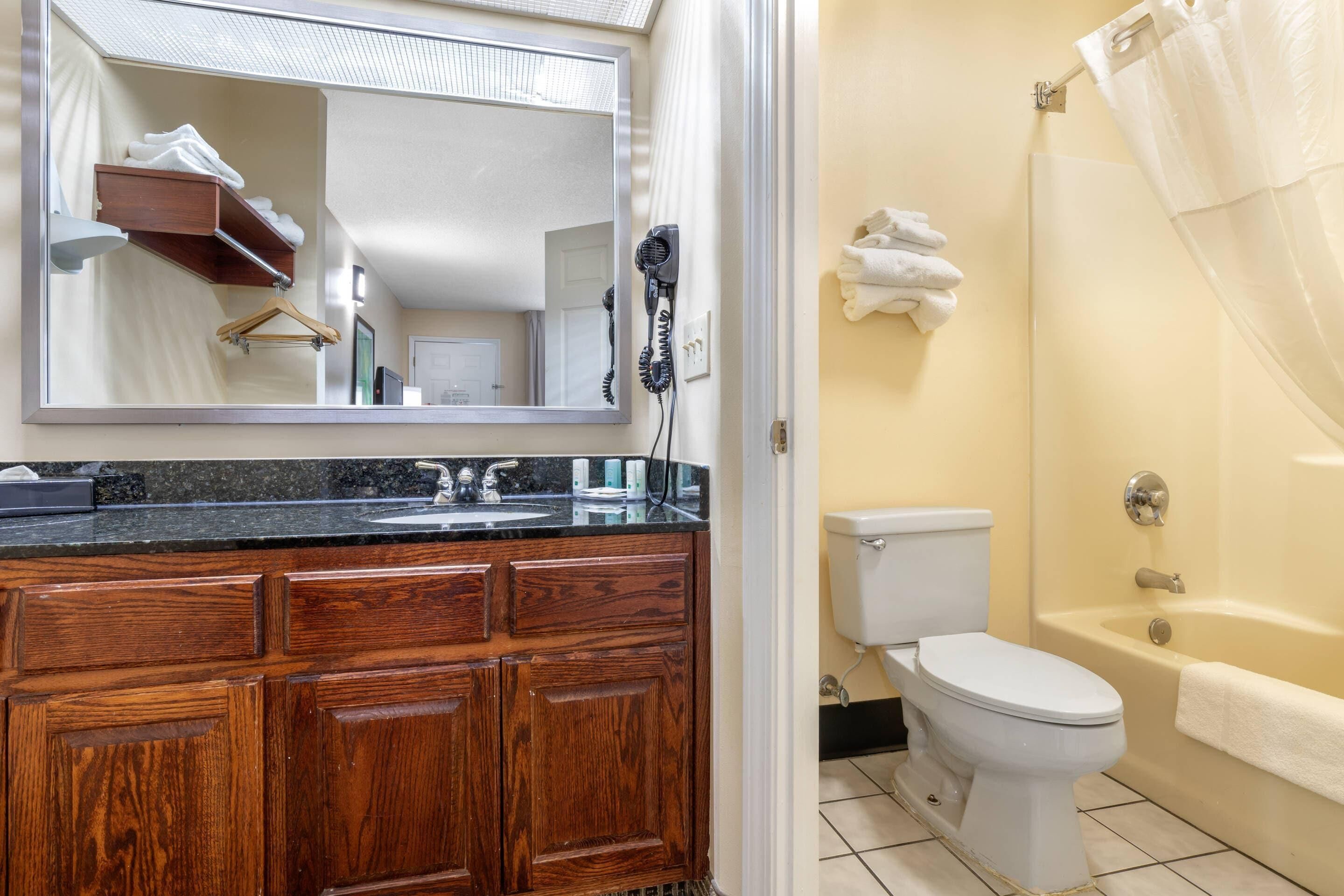 A bathroom with a wooden vanity, a mirror, a hairdryer, a toilet, and a bathtub.