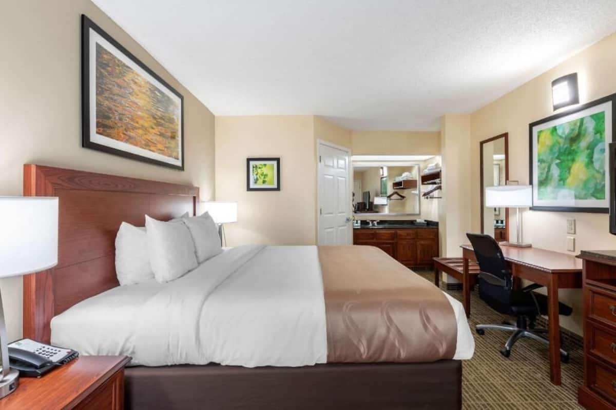 Quarto de hotel com cama, escrivaninha, cadeira e espelho.