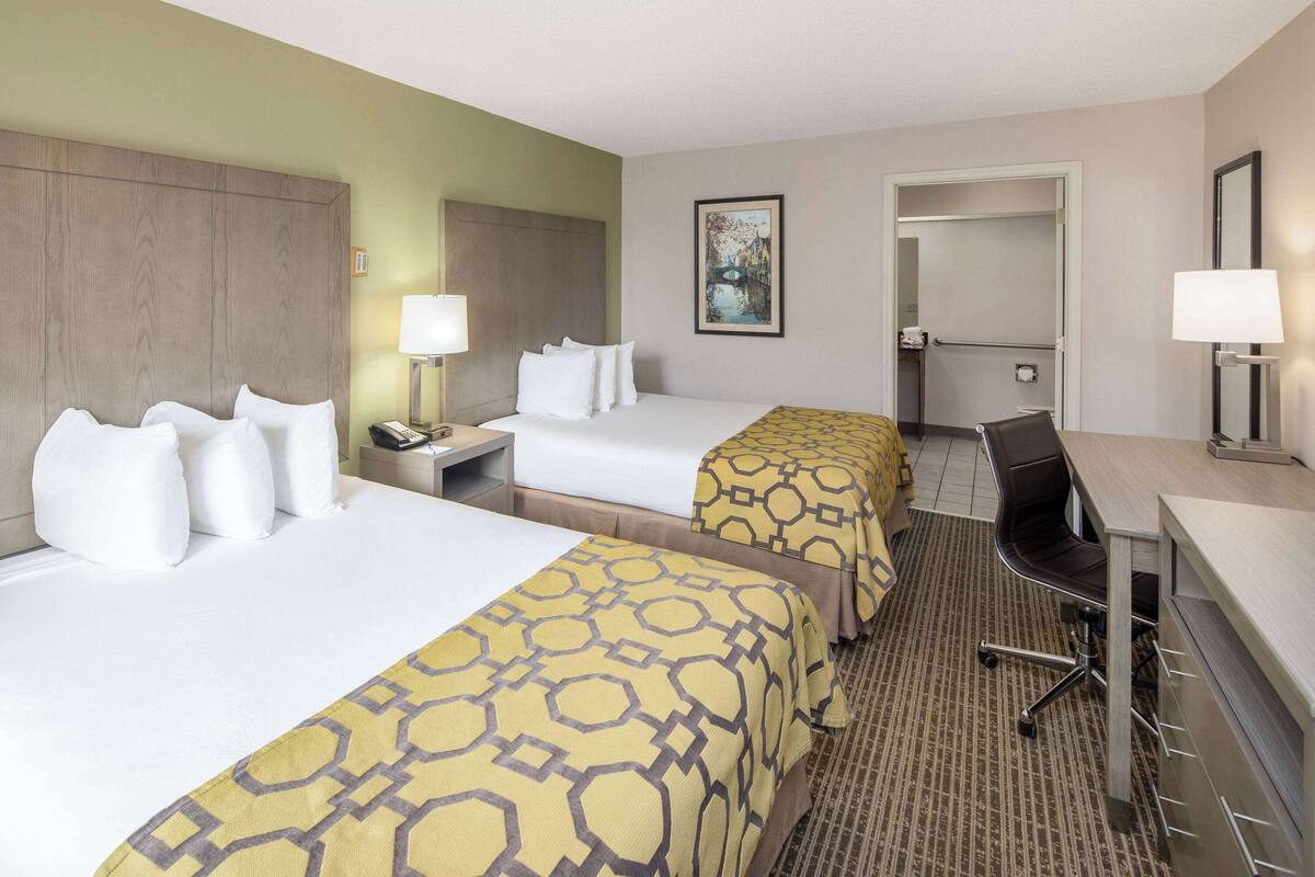 A hotel room with two beds, a desk, a chair, and a bathroom.