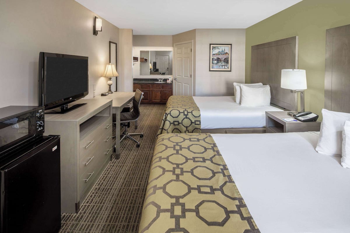 A hotel room with a TV, desk, two beds, a small kitchenette, and a bathroom.