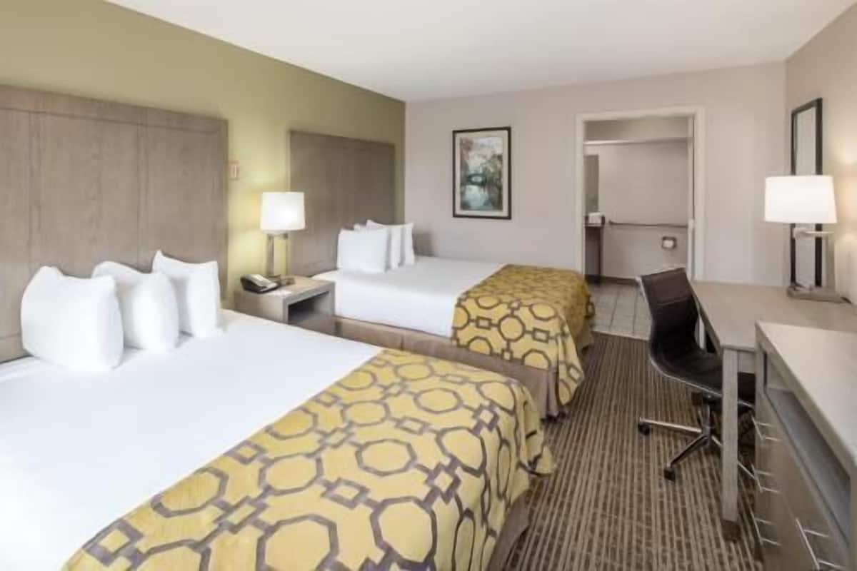 A hotel room with two beds, a desk, a chair, a lamp, and a painting on the wall.