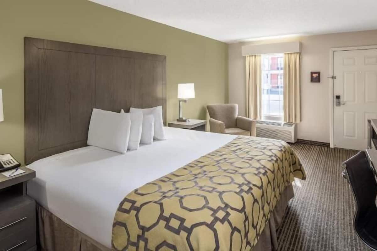 A hotel room with a large bed, a desk with a computer, a chair, a TV, and a window with curtains.