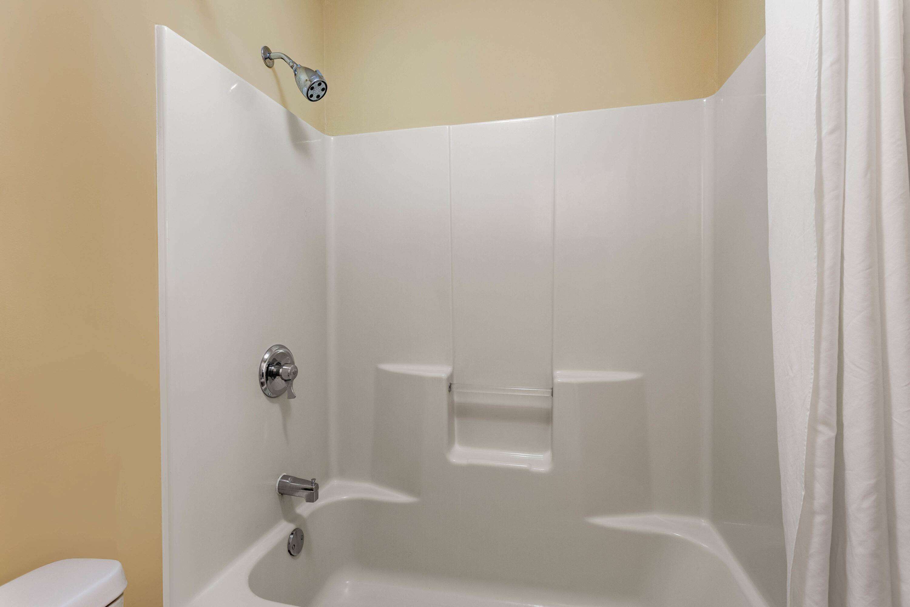 A corner shower with white tiles, a toilet, and a shower curtain.
