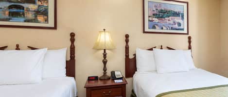 A hotel room with two beds, a nightstand with a lamp, a clock, and a phone.