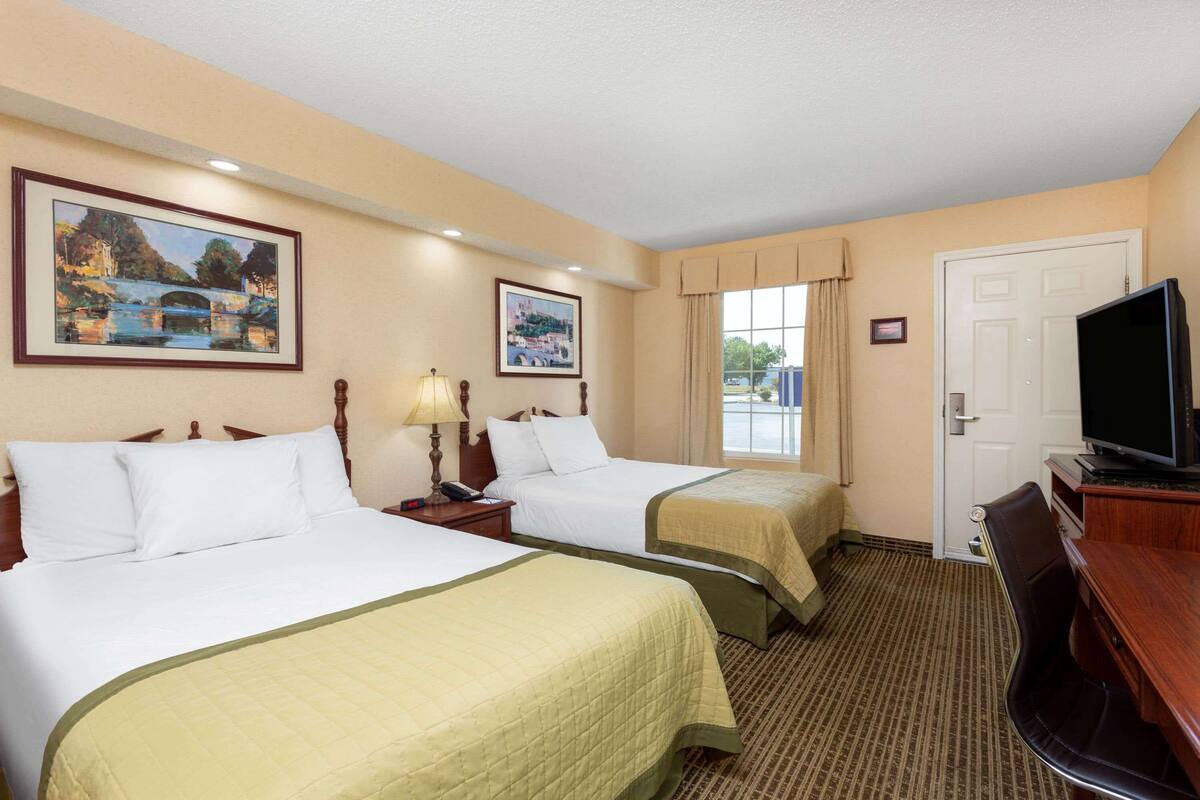 Habitación de hotel con dos camas, televisión, escritorio y ventana con cortinas.