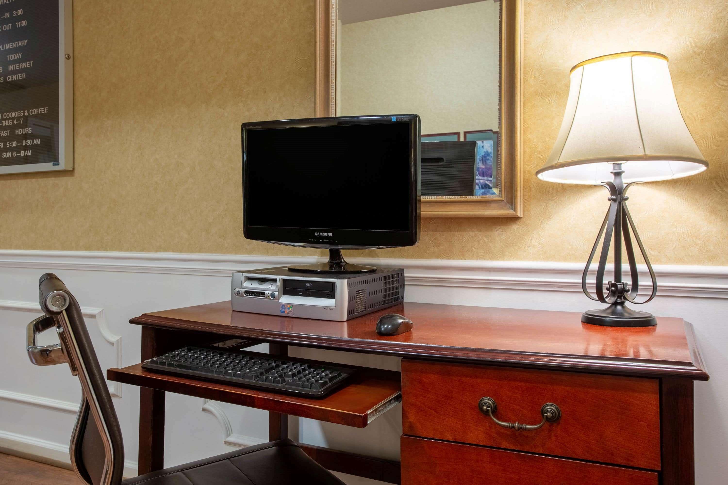 Ein Hotelzimmer mit einem Holztisch, einem Computer, einer Lampe und einem Stuhl.