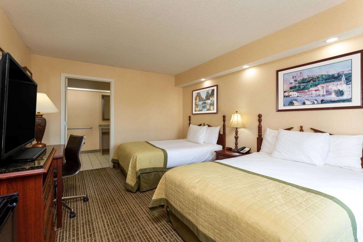 Habitación de hotel con dos camas, un escritorio con computadora, un televisor y una lámpara.