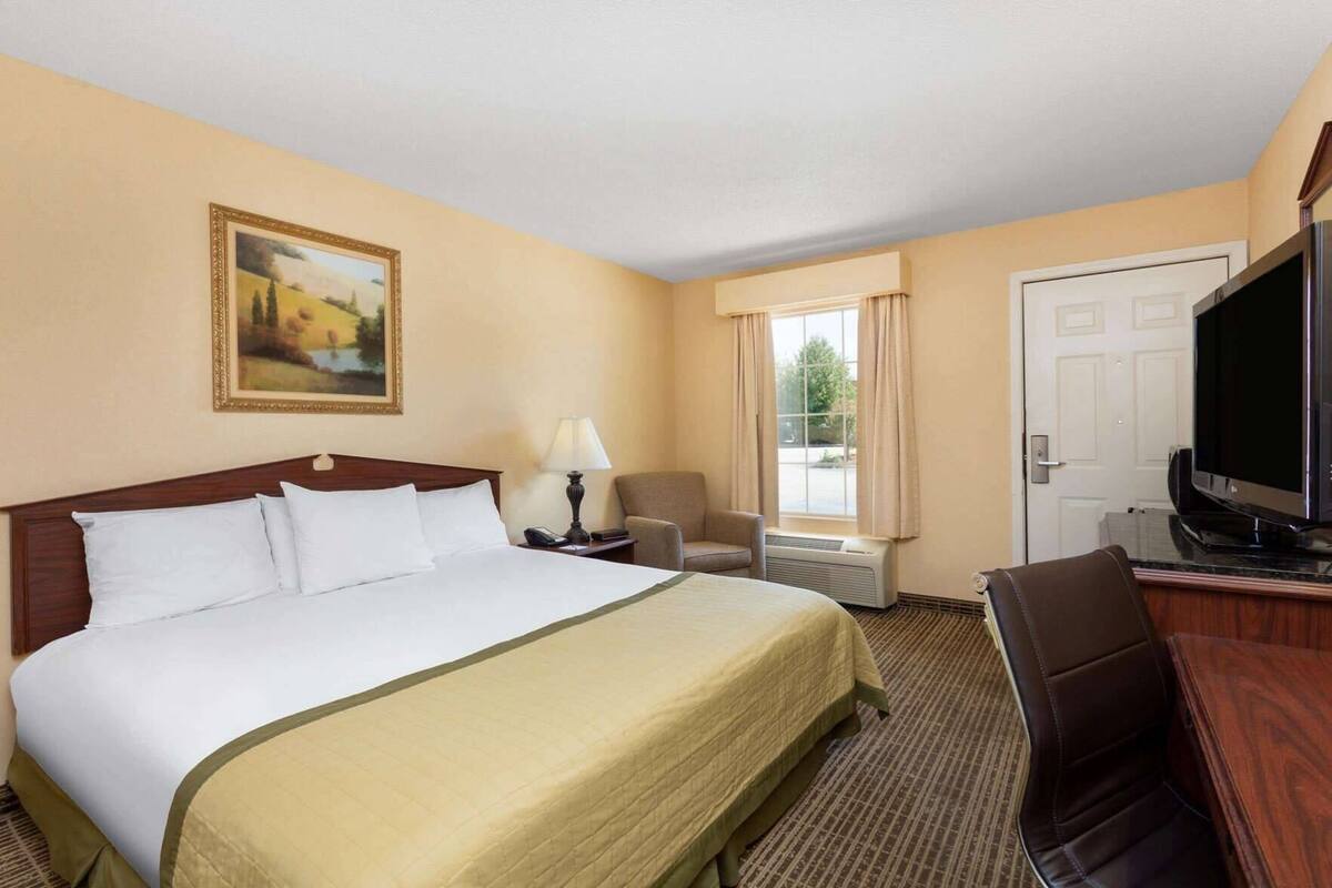 Una habitación de hotel con una cama, un escritorio, un televisor y una ventana con cortinas.