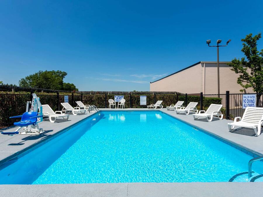 A swimming pool with lounge chairs and a lifeguard chair, surrounded by a fence and a building.