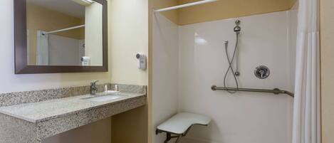 A bathroom with a granite countertop sink, a mirror, a shower with a grab bar, and a ceiling light.