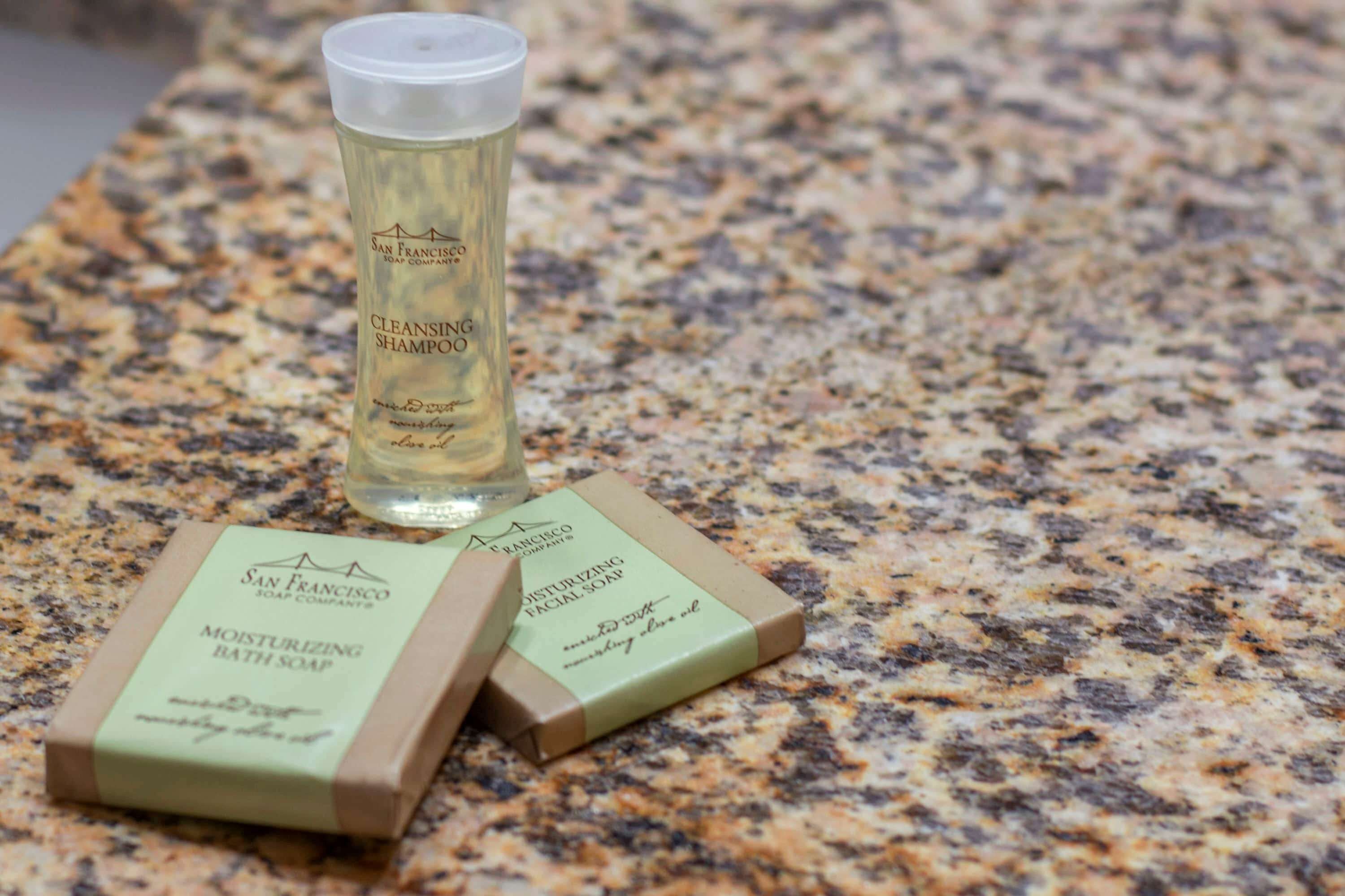 A bottle of cleansing shampoo and two bars of moisturizing bath soap on a granite countertop.