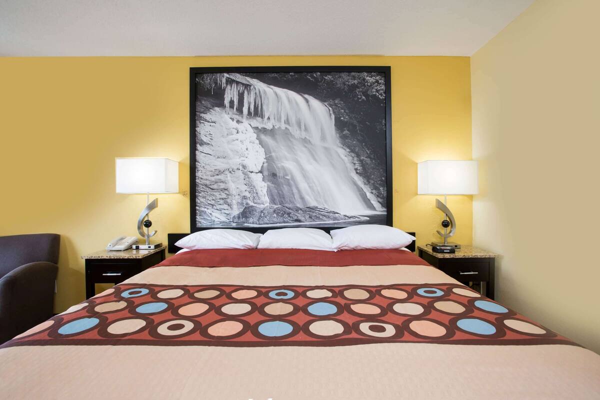 Una camera d'albergo con un letto, due lampade sui comodini, un telefono e una grande fotografia di una cascata sulla parete.