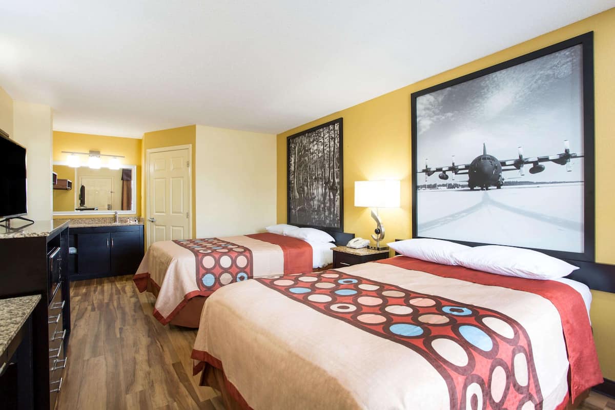 Camera d'albergo con due letti, una televisione, una scrivania e un quadro raffigurante un aereo.