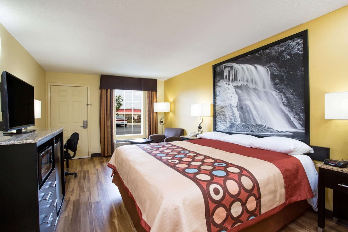 Una camera d'albergo con un letto, una scrivania con televisore, una poltrona, una finestra con tende e un grande quadro raffigurante una cascata.
