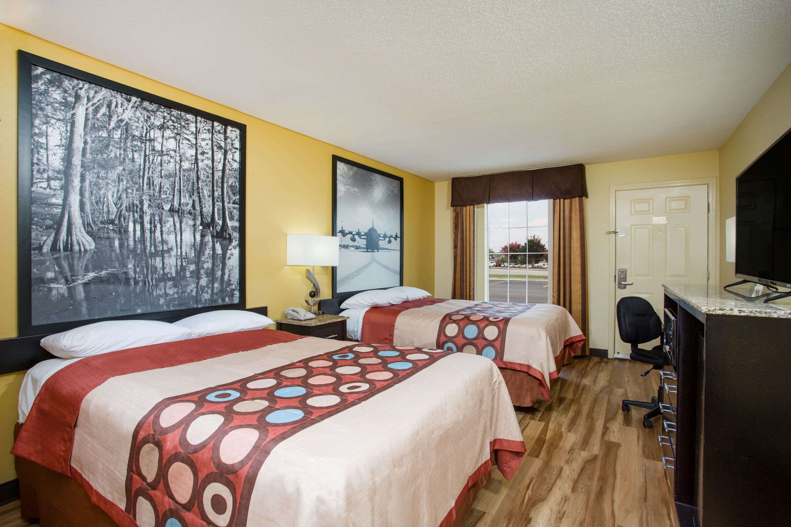 A hotel room with two beds, a desk, and a TV.