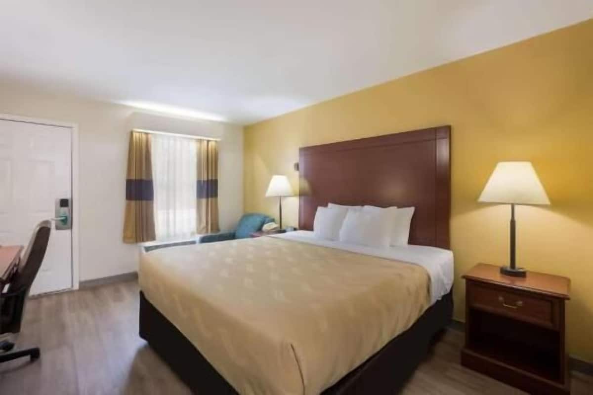Ein Hotelzimmer mit einem Bett, zwei Nachttischlampen, einem Schreibtisch und einem Sessel.