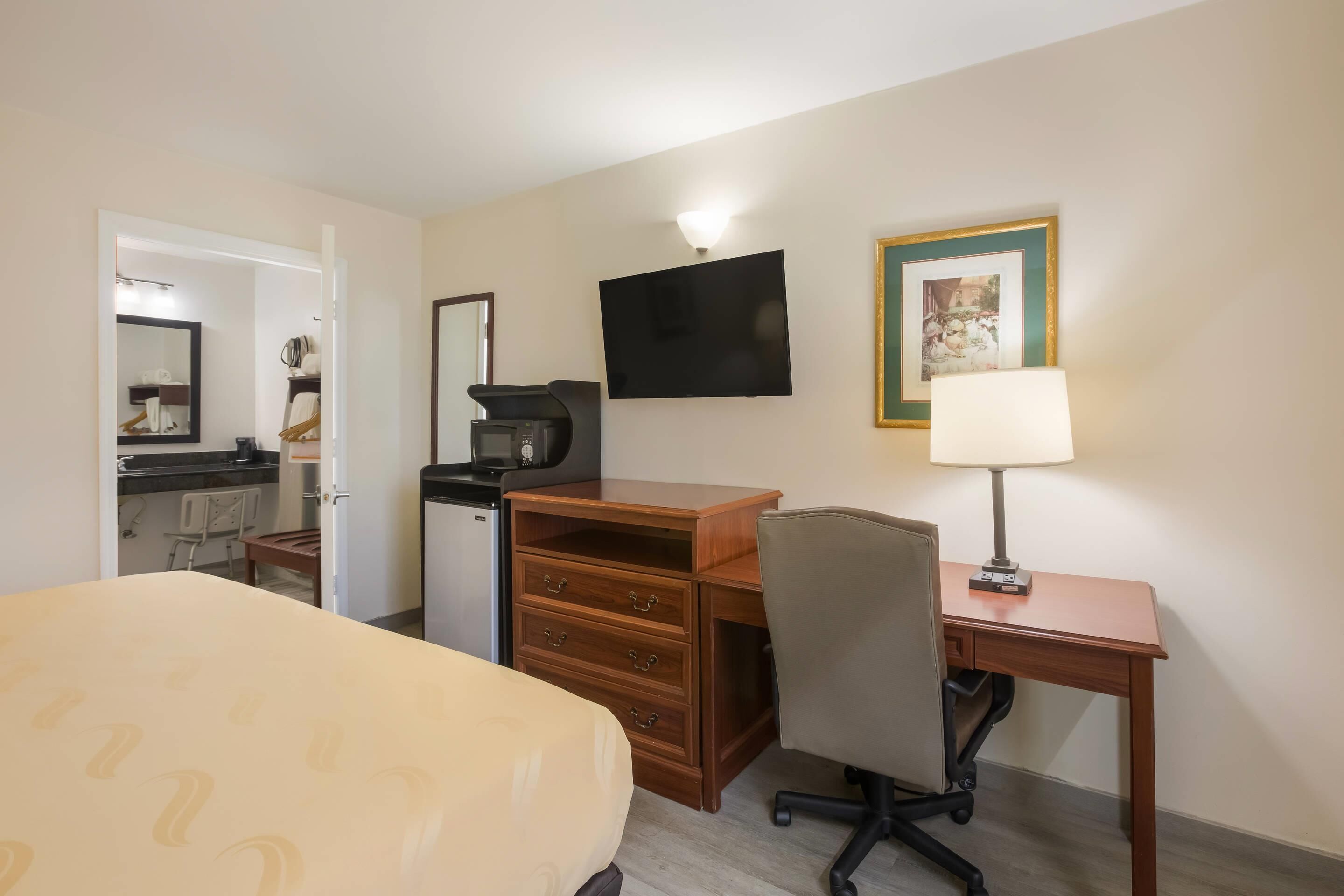 Habitación de hotel con cama, escritorio con silla, cafetera, televisor y un cuadro en la pared.