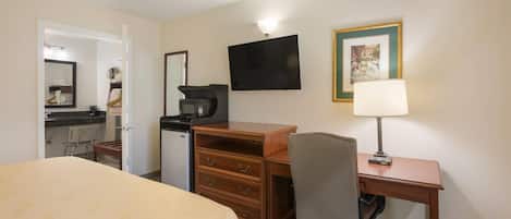 Habitación de hotel con cama, escritorio con silla, cafetera, televisor y un cuadro en la pared.