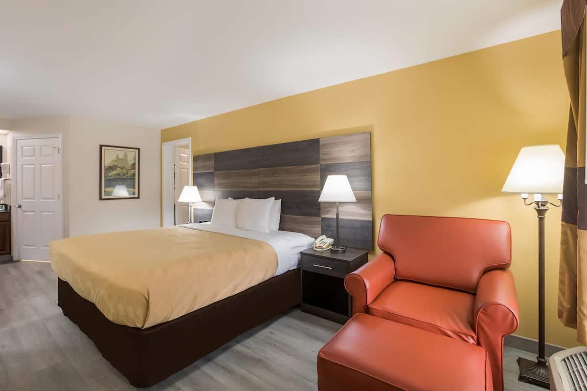 Ein Hotelzimmer mit einem großen Bett, einem roten Ledersessel, zwei Nachttischen mit Lampen, einem hölzernen Kopfteil und einer Tür.