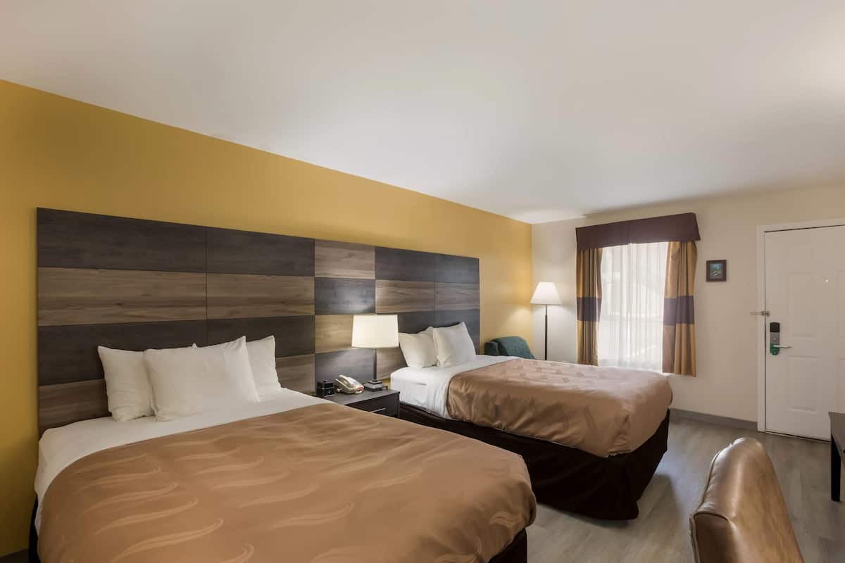 Ein Hotelzimmer mit zwei Betten, einem Holzkopfstück, einem Nachttisch mit Lampe und einer Tür mit Schloss.