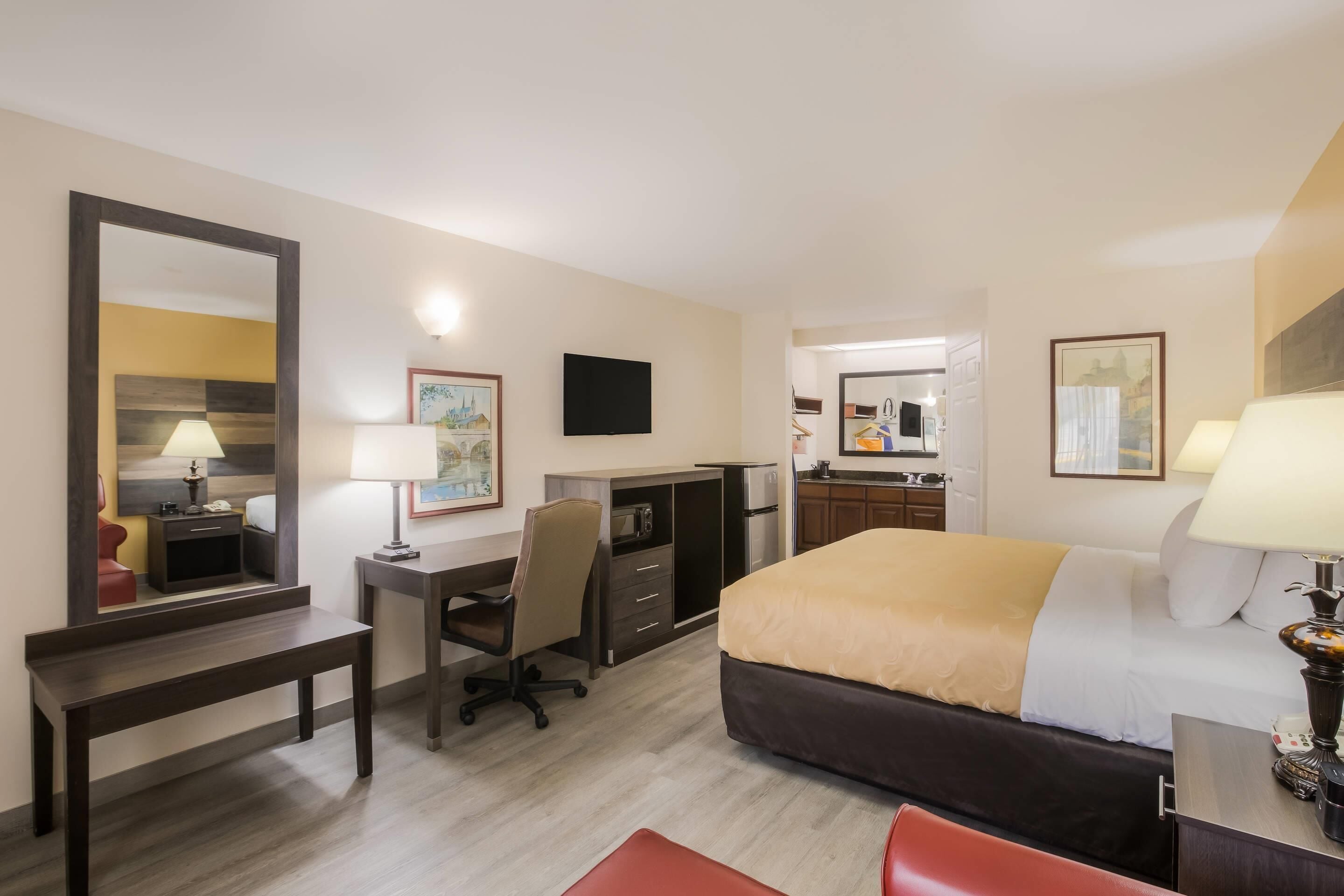 A hotel room with a bed, desk, chair, and a large mirror.