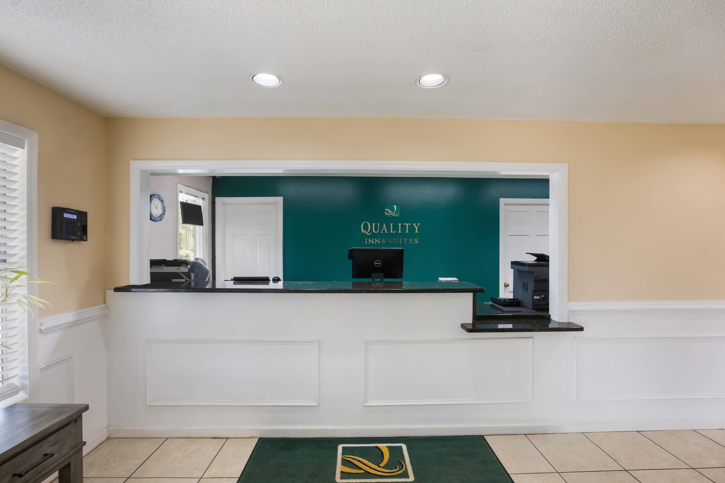 A reception desk with a green backdrop and "Quality Inns & Suites" branding.