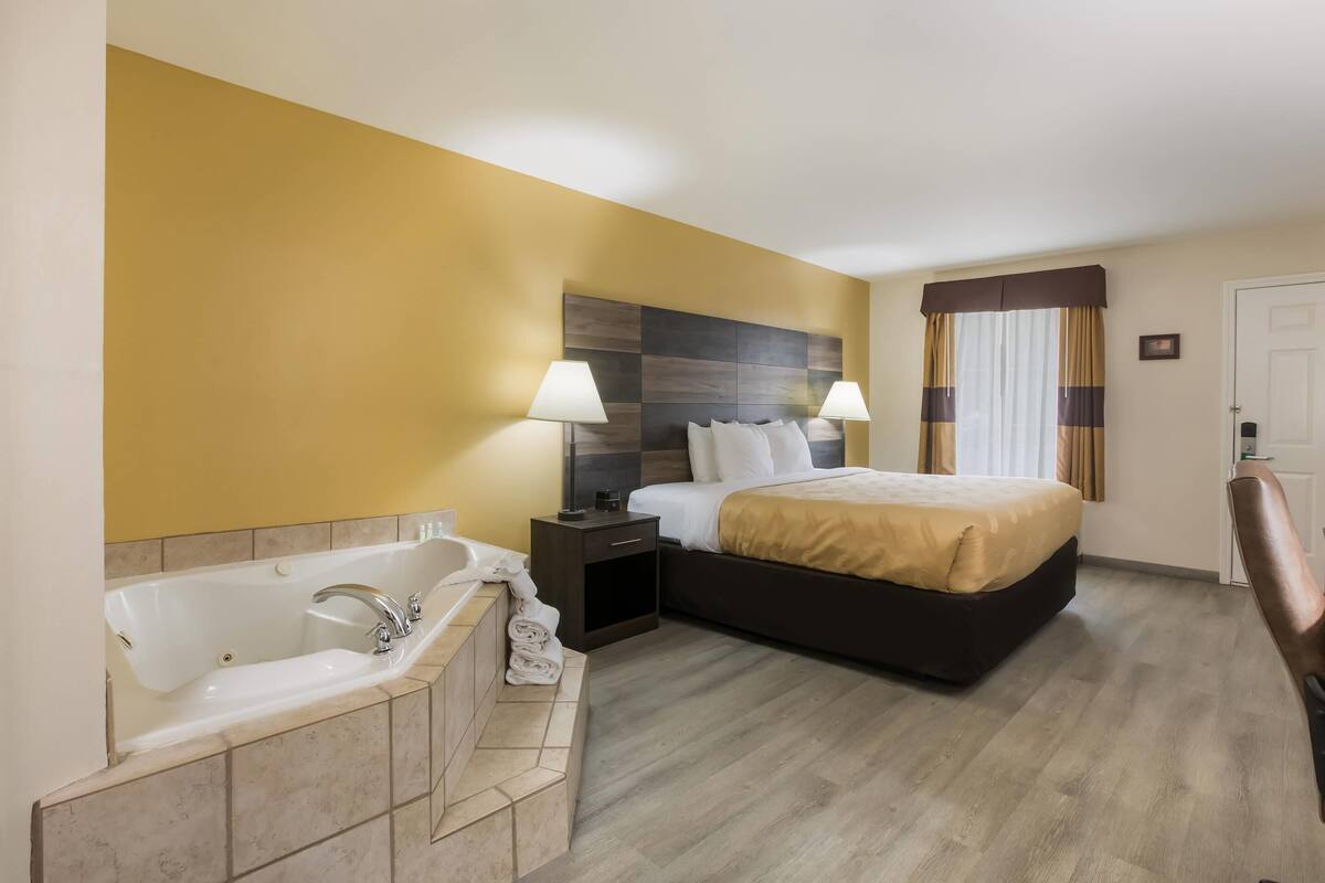Ein Hotelzimmer mit einem großen Bett, einem eigenen Badezimmer mit Badewanne und einem Schreibtisch mit Lampe.