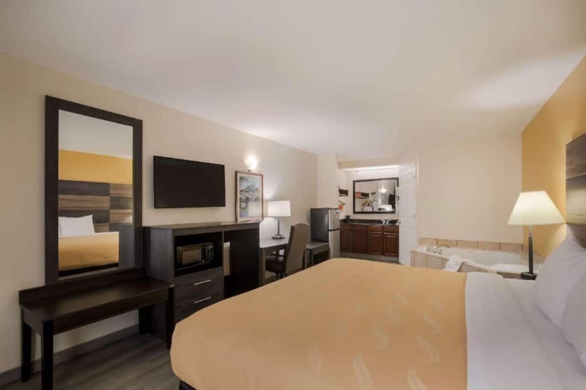 Ein Hotelzimmer mit Bett, Schreibtisch, Stuhl, Fernseher, Spiegel und einer Küchenzeile.