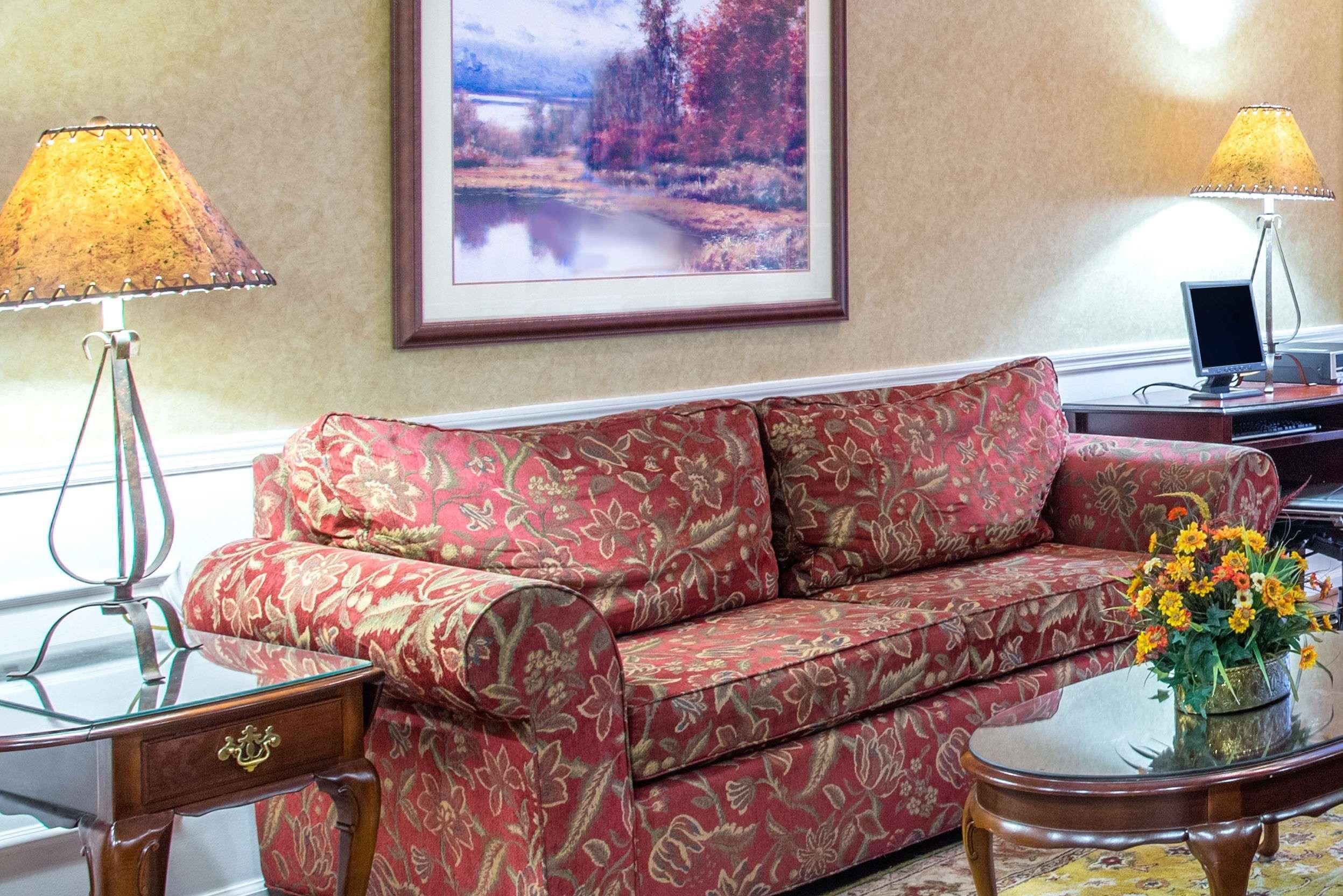 Un soggiorno con un divano rosso a motivi, due lampade, un quadro appeso e un tavolino con un vaso di fiori.