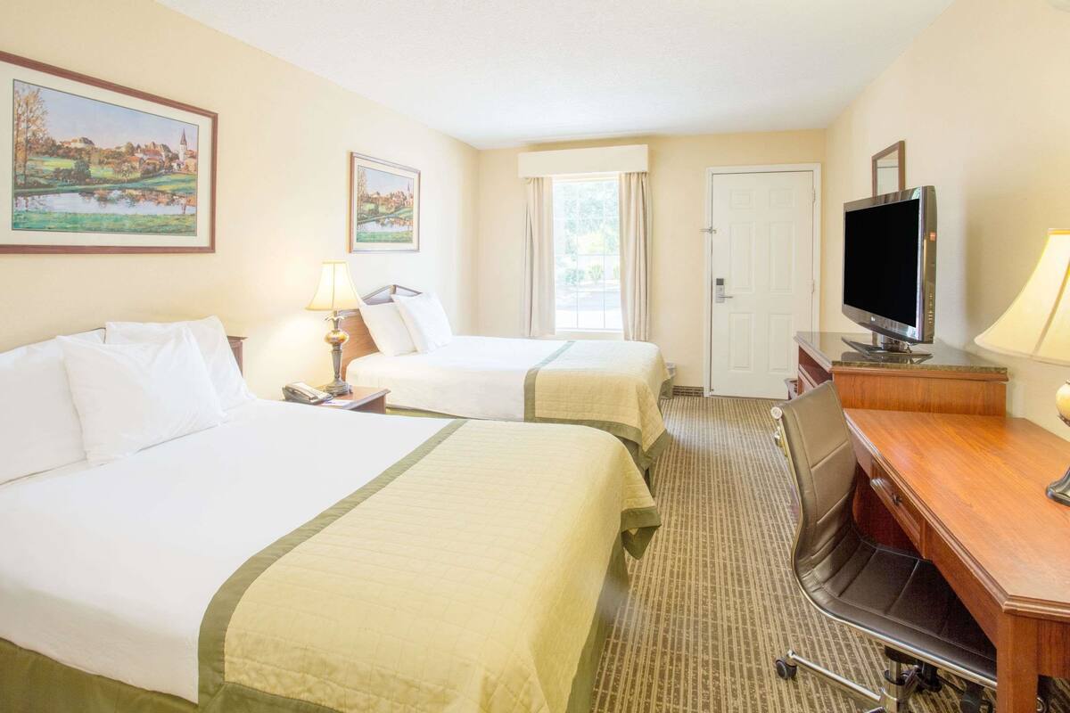 A hotel room with two beds, a desk, a television, and a window with curtains.