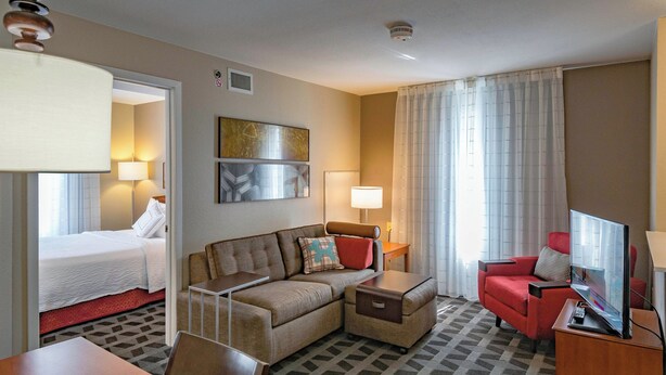 A hotel room with a bed, a sofa, a red armchair, a TV, and a lamp. - Towneplace Suites By Marriott Streetsboro (Streetsboro)