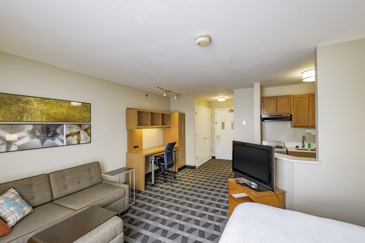 Habitación de hotel con sofá, escritorio, silla, televisión y kitchenette.