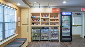 A small room with a bench, a refrigerator stocked with beverages, and shelves with snacks. - Towneplace Suites By Marriott Streetsboro (Streetsboro)