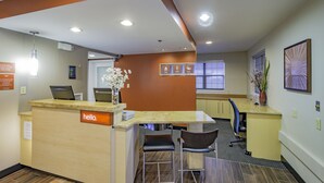 A reception area with a 'hello' sign, a counter, two chairs, and a vase with flowers. - Towneplace Suites By Marriott Streetsboro (Streetsboro)