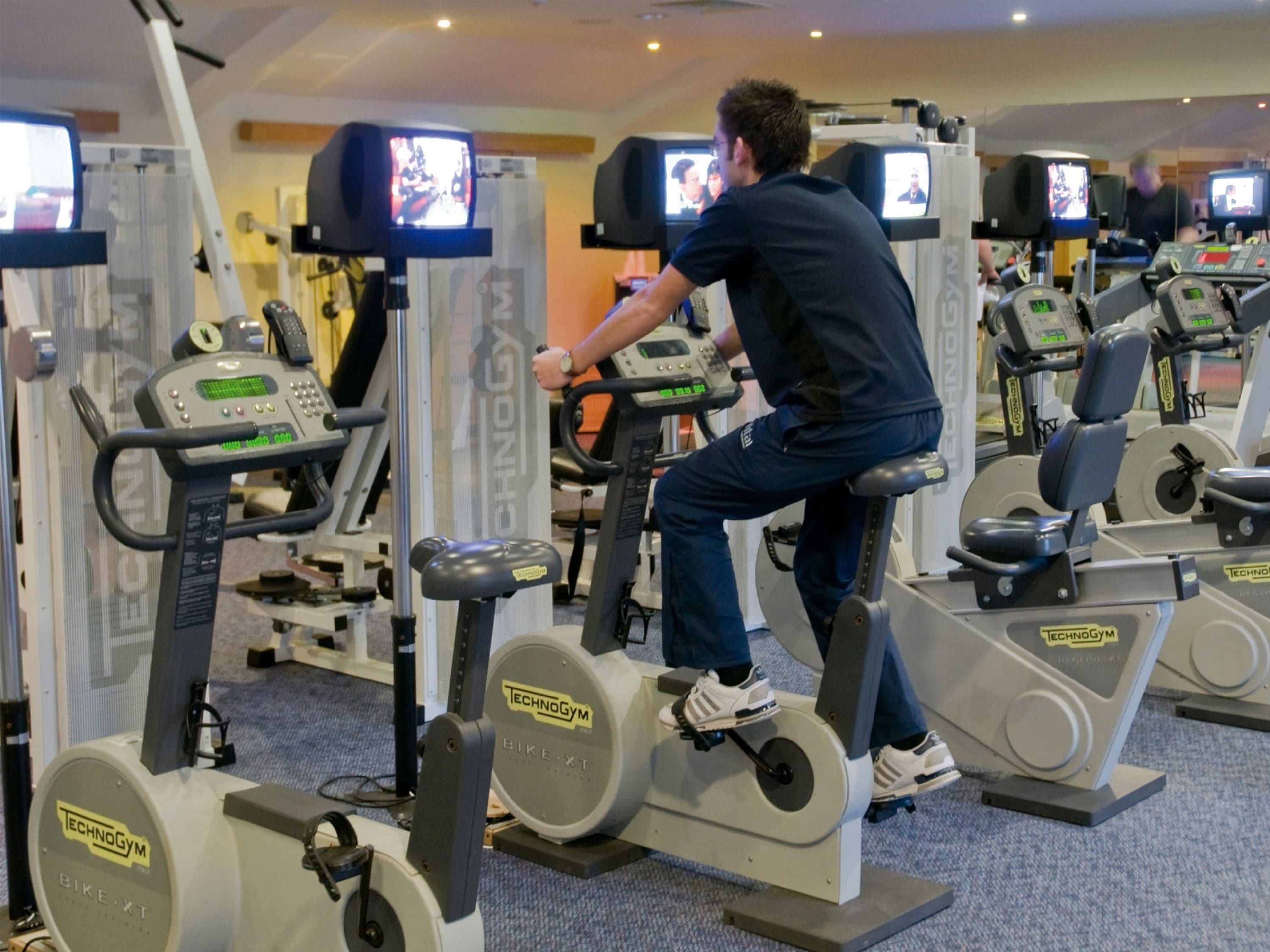 A gym with stationary bikes and televisions mounted on the walls.