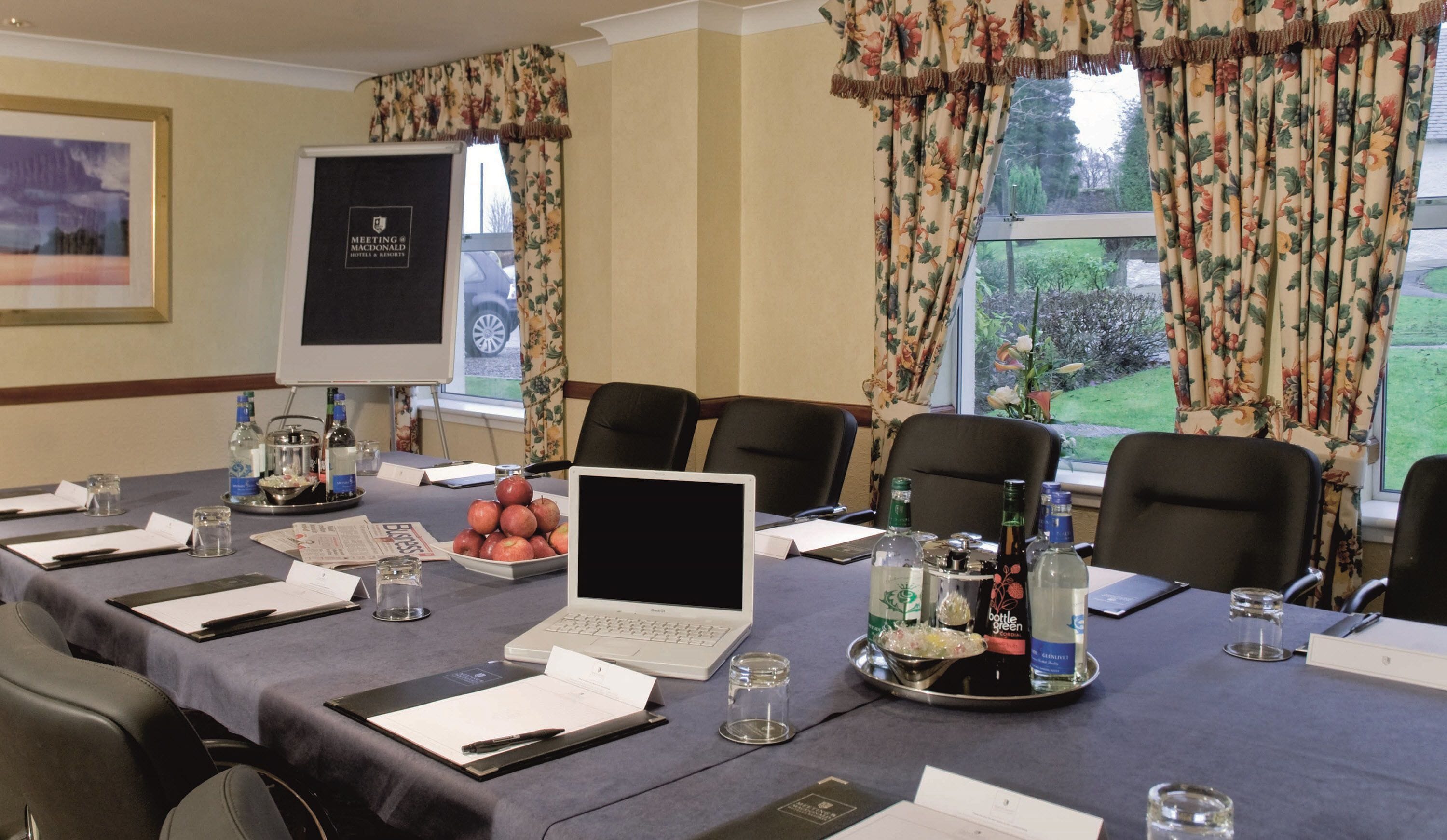 A meeting room with a laptop, documents, and a projector screen.