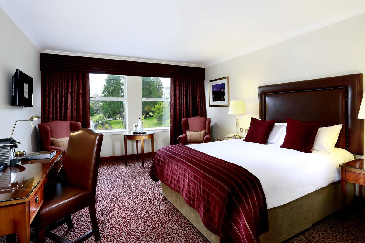 Ein Hotelzimmer mit einem großen Bett, zwei Sesseln, einem Schreibtisch und einem fenster mit Vorhängen.