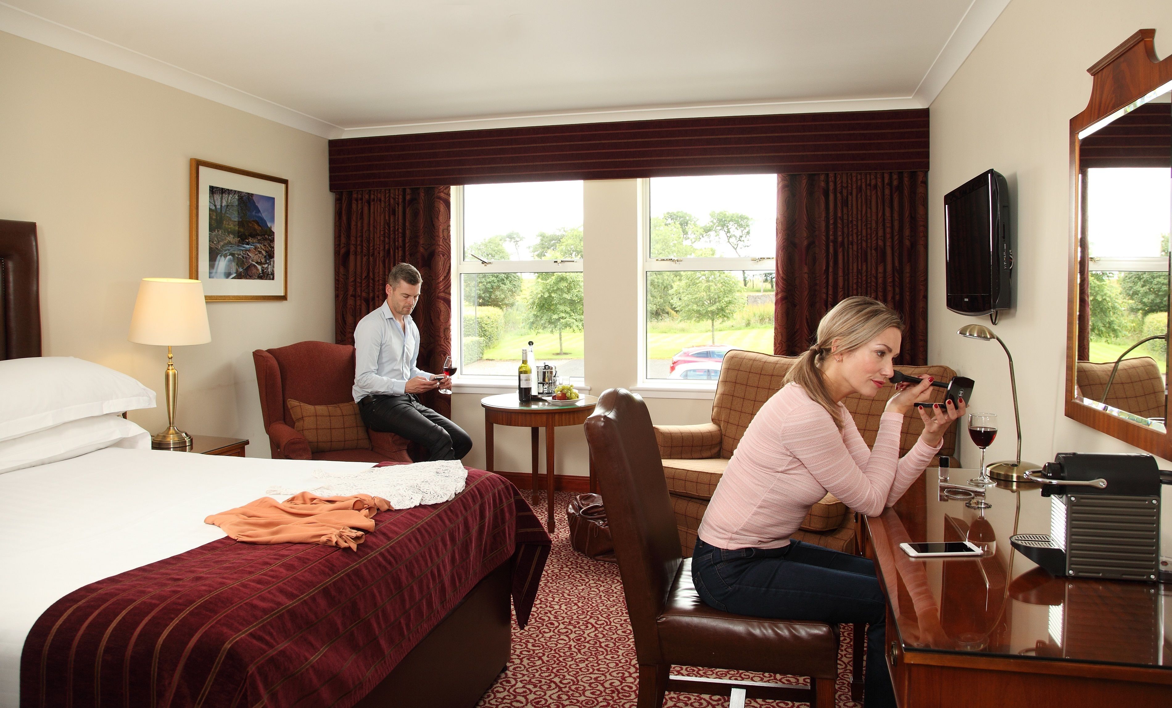 Habitación de hotel con cama, zona de estar con mesa, televisión y ventana con cortinas.