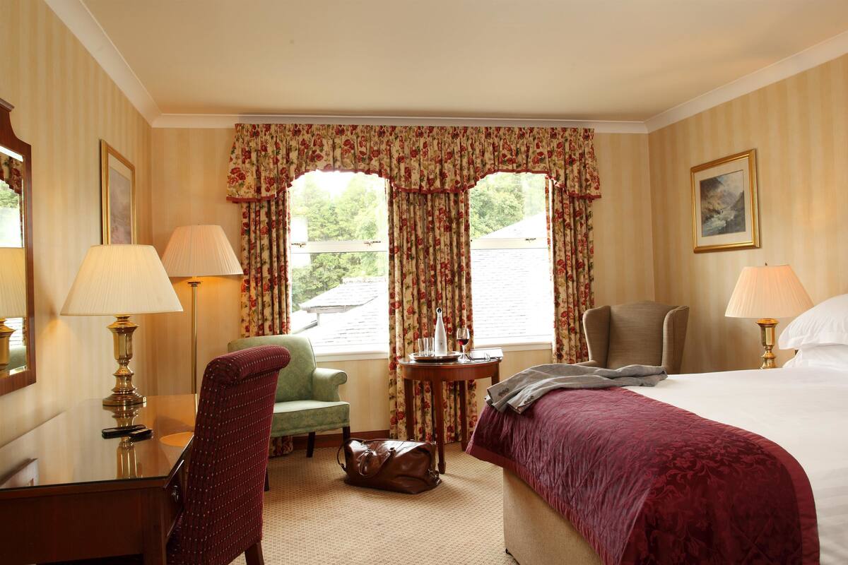 Ein Hotelzimmer mit einem Bett, zwei Stühlen, einem Schreibtisch und einem Tisch mit einer Lampe.