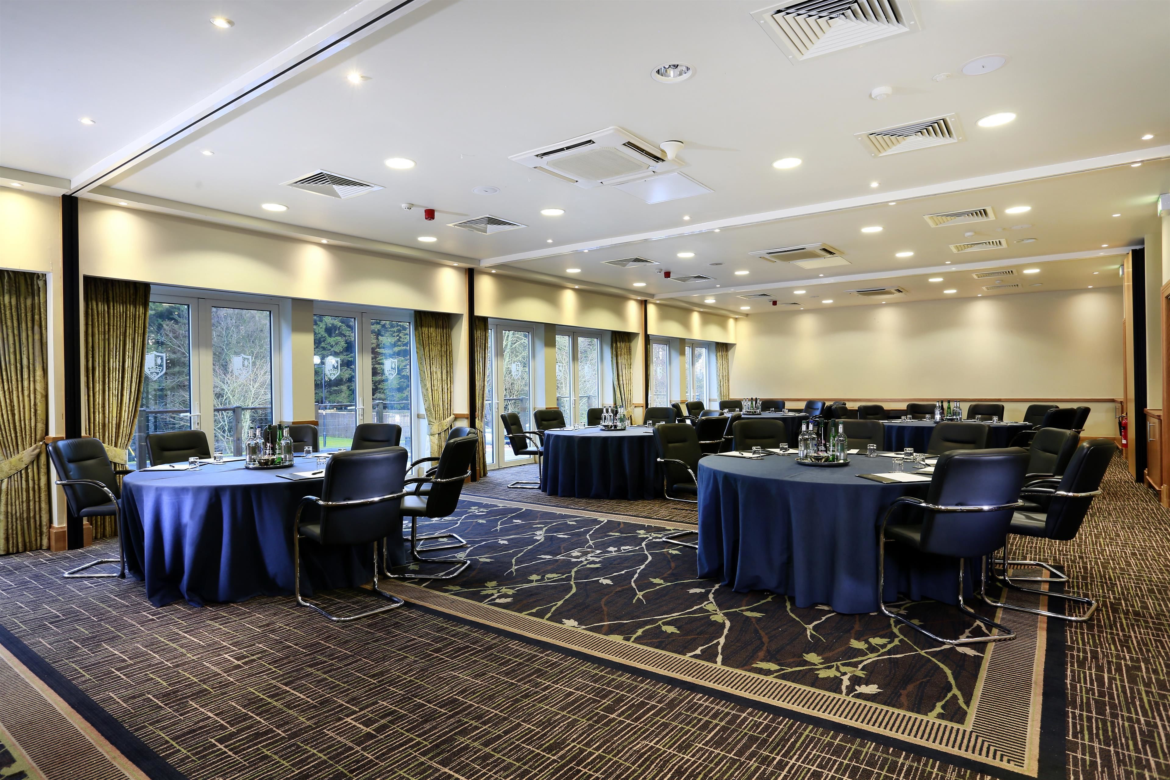 A conference room with multiple tables, chairs, and a carpeted floor.