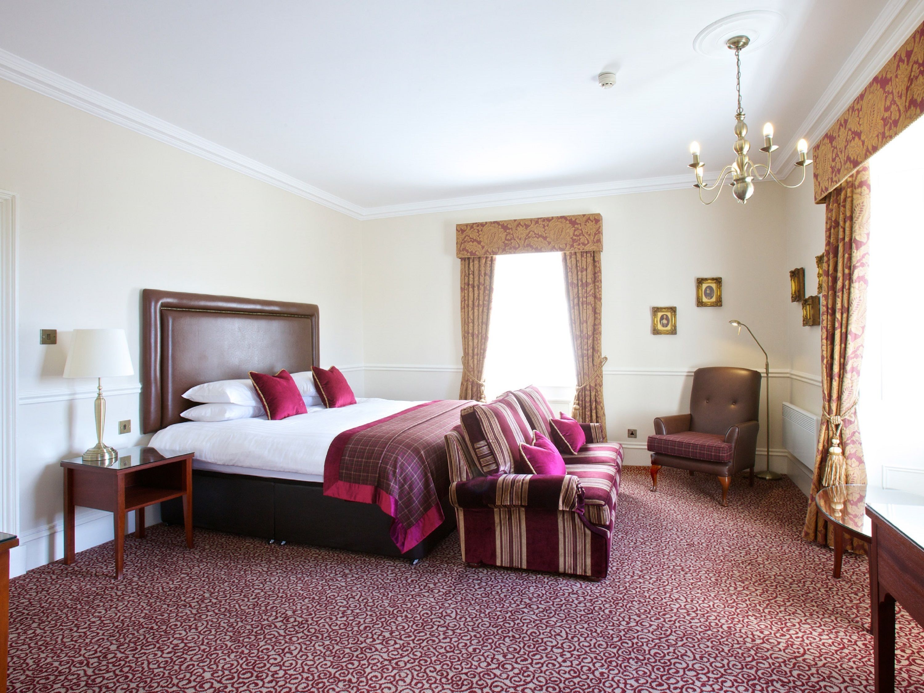 Une chambre d’hôtel dotée d’un grand lit, d’un coin salon avec un canapé et des fauteuils, d’un bureau et d’un lustre.