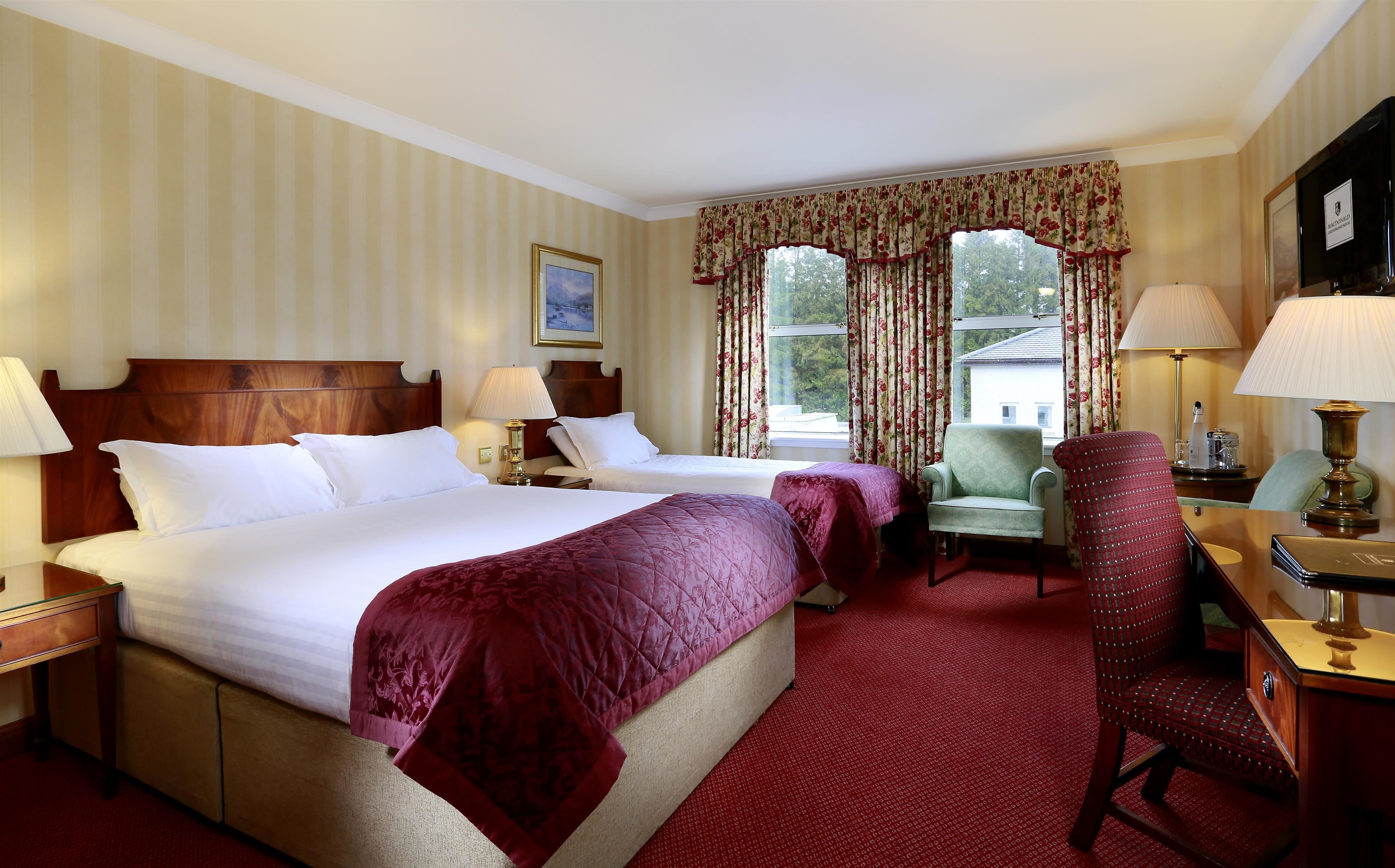 A hotel room with two beds, a desk, a chair, and a window with curtains.