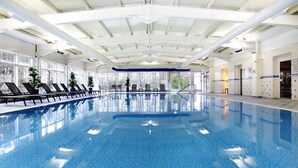 A large indoor swimming pool with clear blue water, surrounded by lounge chairs and potted plants.